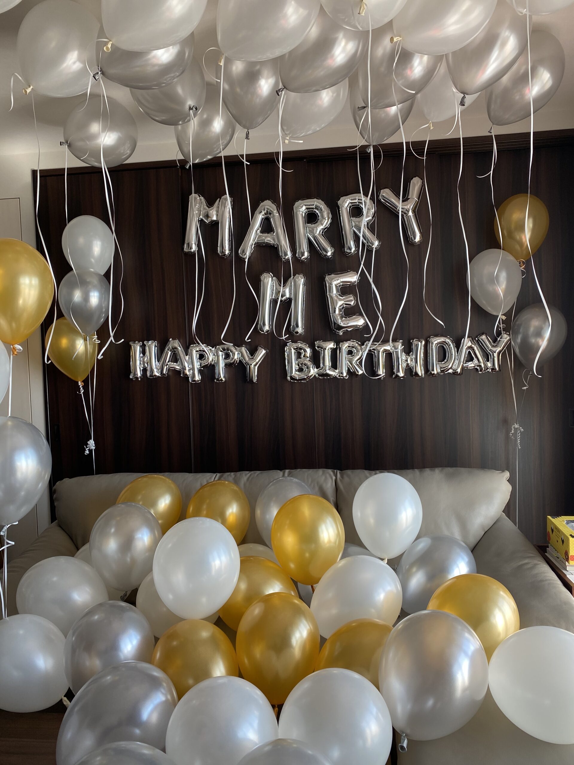 壁に貼り付けたシルバーのアルファベットバルーンでMARRY MEとHAPPY BIRTHDAYのメッセージを作るサプライズ装飾